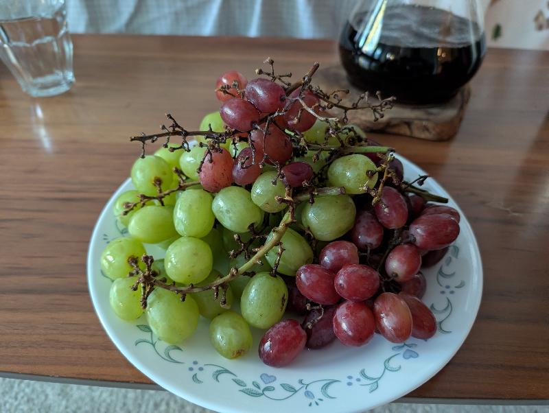 A glass, a seraf with brewing coffee, a pile of grapes